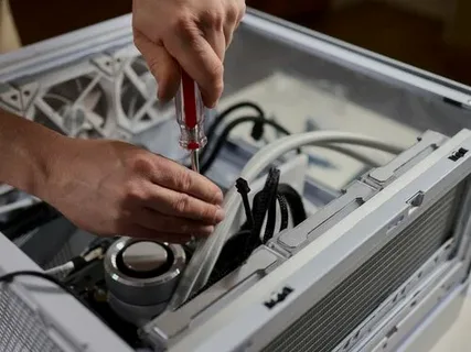 A person uses a red-handled screwdriver to secure a component inside a white appliance housing with visible cooling fans and internal wiring, addressing Common Appliance Problems through professional inspection and repair.